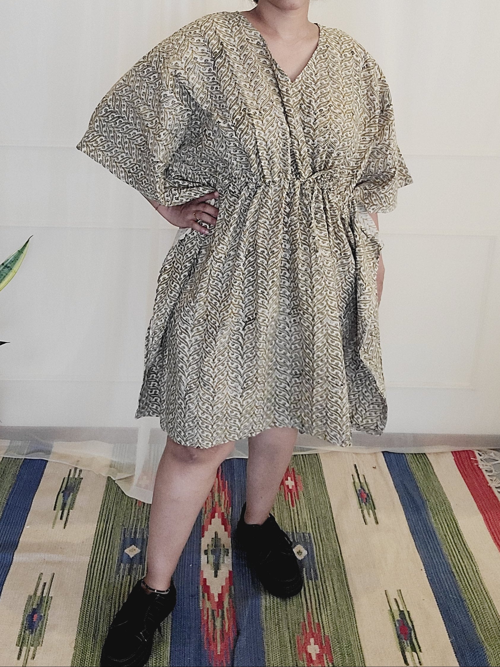 Person wearing a patterned dress standing on a colorful rug with a plant in the background