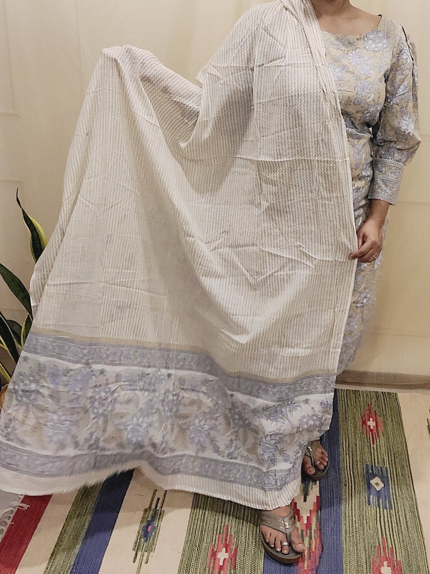 Woman wearing a traditional outfit with a patterned shawl in a room with a colorful rug.