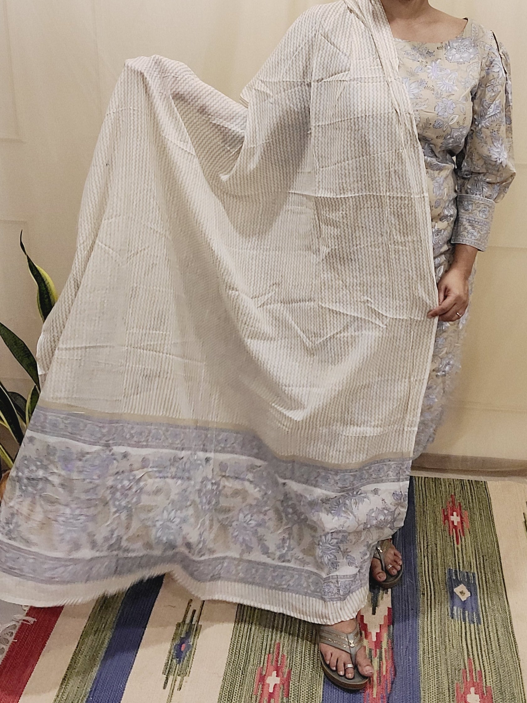 Woman wearing a traditional outfit with a patterned shawl in a room with a colorful rug.