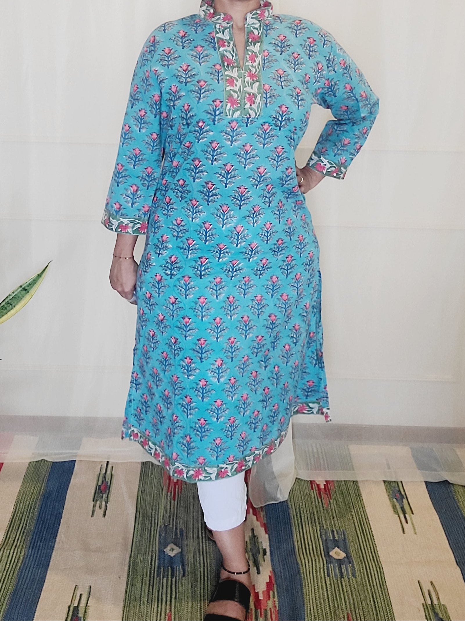 Person wearing a blue floral dress standing on a light-colored floor with a plant in the background.