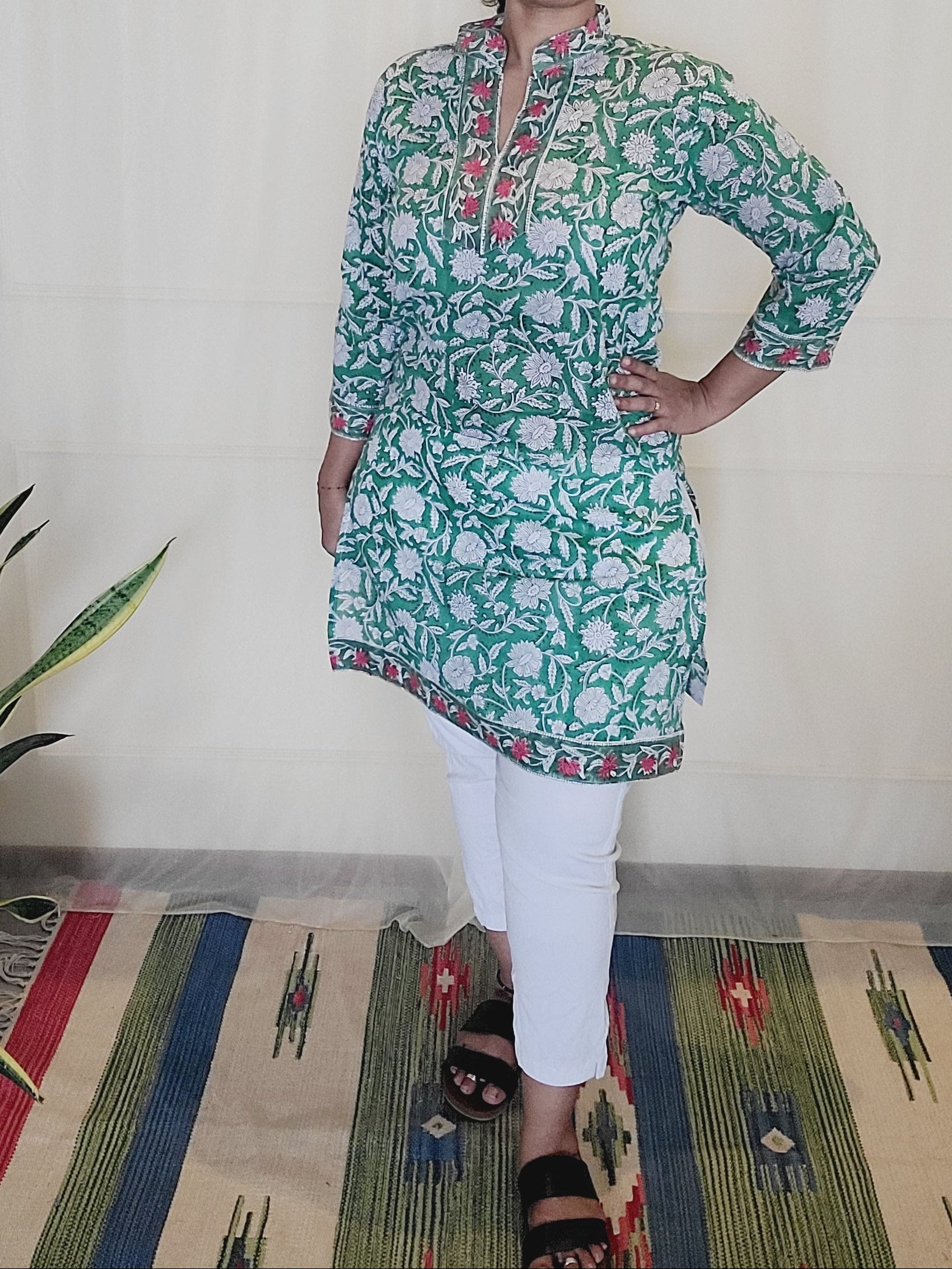 Woman wearing a green floral block printed Kurti standing on a colorful rug.